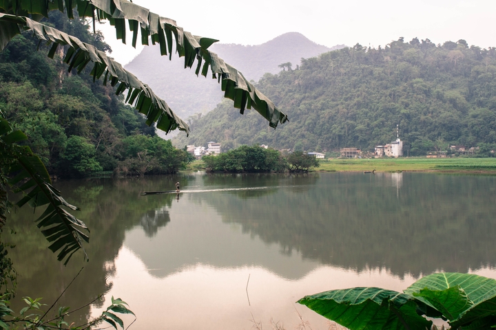       A serene lake surrounded by mountains and greenery with a person on a boat.
  