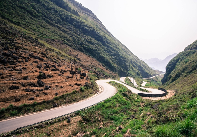       A winding mountain road with green and rocky slopes.
  