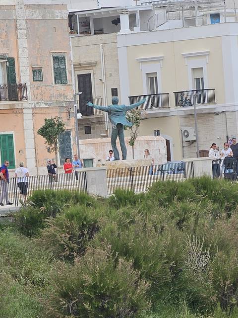 Statue in front of urban buildings with greenery.