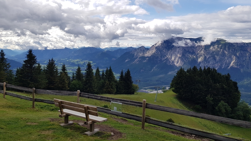Bench overlooking a mountainous landscape with clouds.