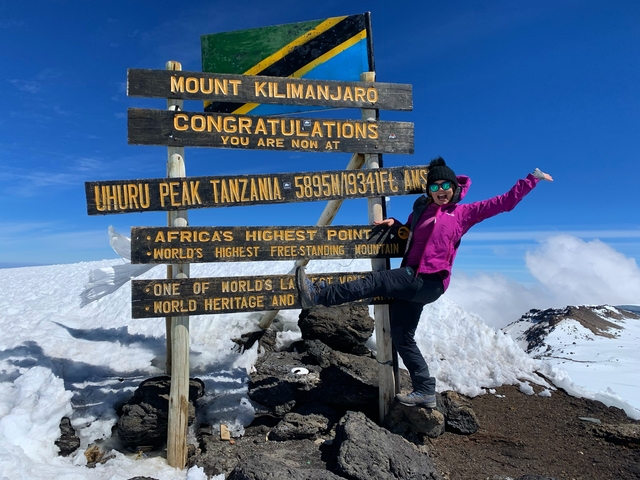 Person celebrating at the sign of Uhuru Peak, Mount Kilimanjaro.