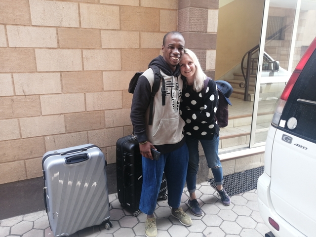Two people posing with luggage outside a building.