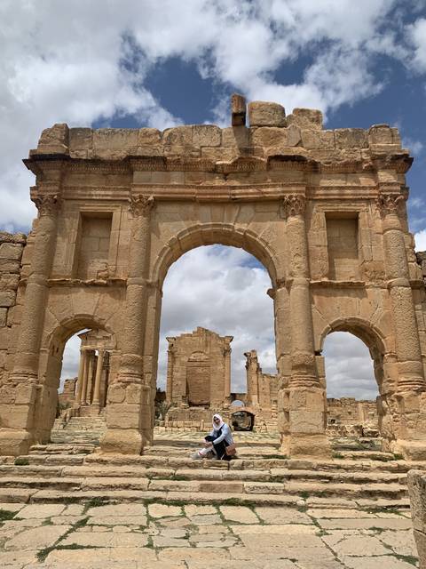      Person sitting in front of ancient Roman ruins.
  