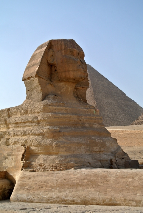 Close-up view of the Sphinx with a pyramid in the background.
