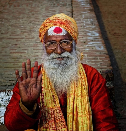       Elderly man with traditional attire waving and smiling.
  