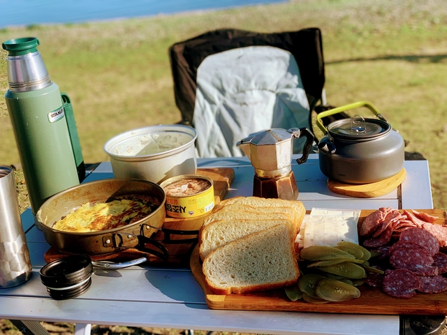 Outdoor picnic setup with various foods and drinks on a table.