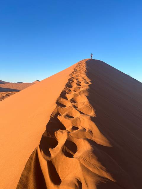 Footprints along a steep sand dune.