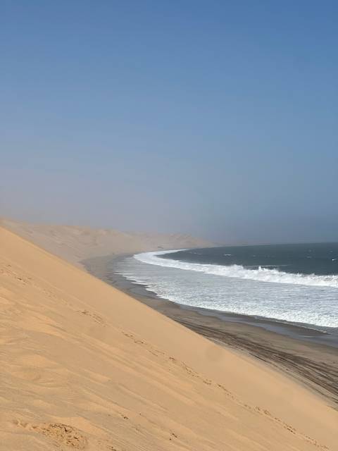 Sand dunes meeting the ocean with waves crashing.