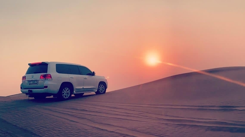       SUV on a sand dune with a sunset in the background
  