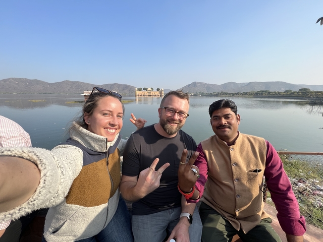 Group of people posing by a lake with a palace in the background.