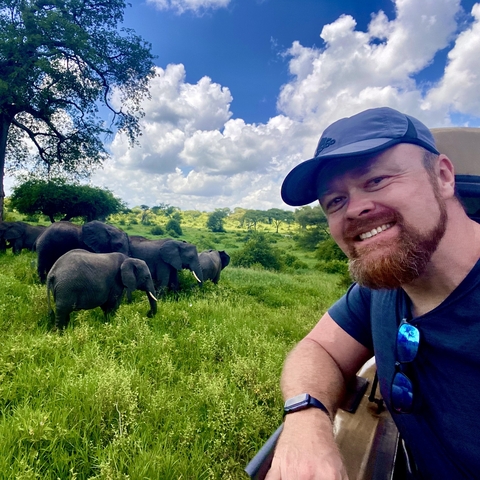       Selfie with elephants in the background in a green landscape.
  