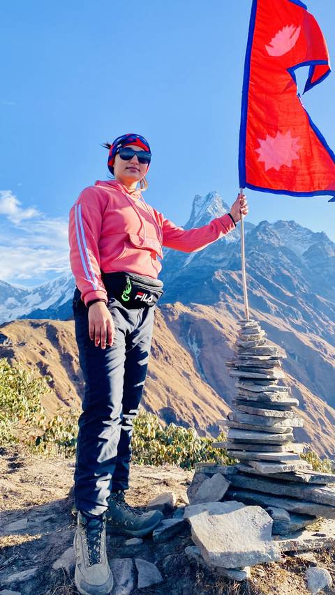 Person posing with a cairn in a mountainous landscape.