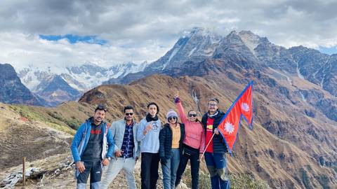 Group of people posing with flags in a mountainous area.