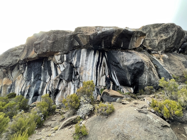 Person standing in front of a large rock formation with streaked patterns.