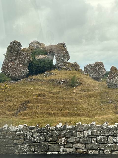 Ruins of a stone structure against a grassy hill.