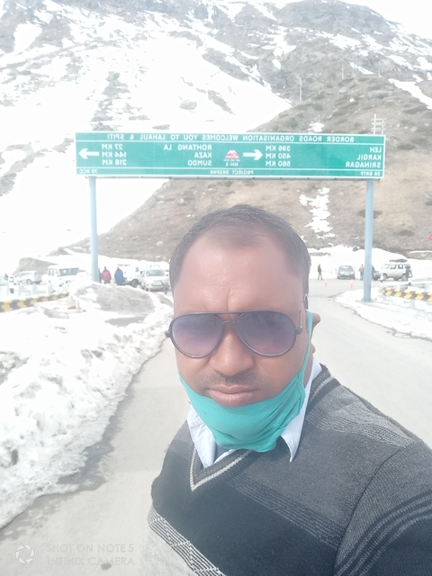 Selfie with snow-covered mountains and cars in the background.