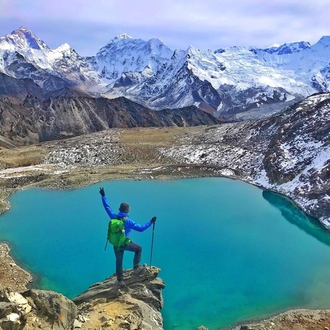       Person standing triumphantly at a mountain summit overlooking a turquoise lake.
  