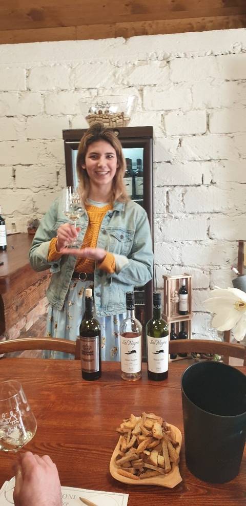       Person holding a glass inside a winery setting with wine bottles on the table.
  