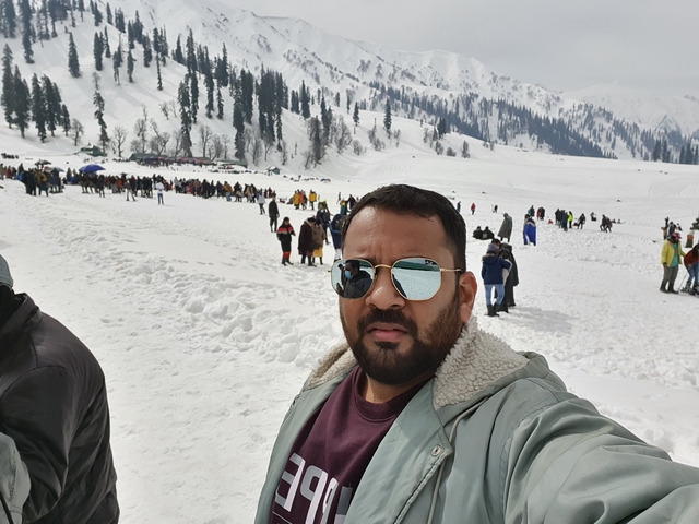 Person taking a selfie in a snowy landscape with crowds.