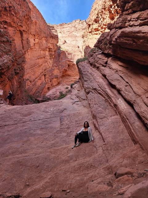 Person posing on red rock formations with clear blue sky above.