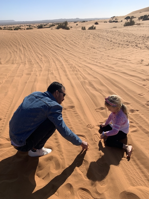       Man and child sitting on sand dunes.
  