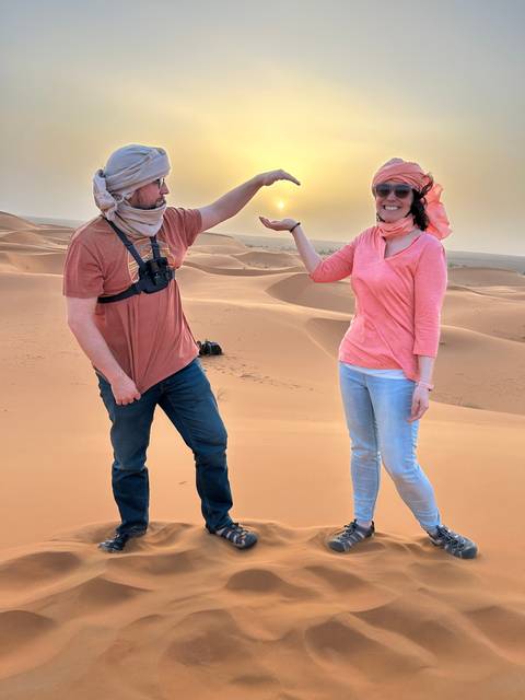 Two people posing on sand dunes at sunset.
