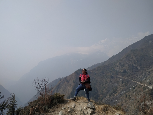       Person posing on a hill with mountain views in the distance.
  