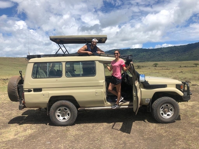       Couple standing by a safari jeep enjoying the scenery.
  