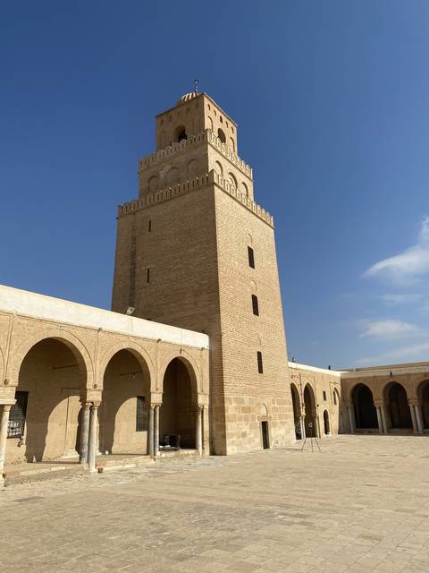       A historic mosque with a tall minaret and arches under a clear sky.
  