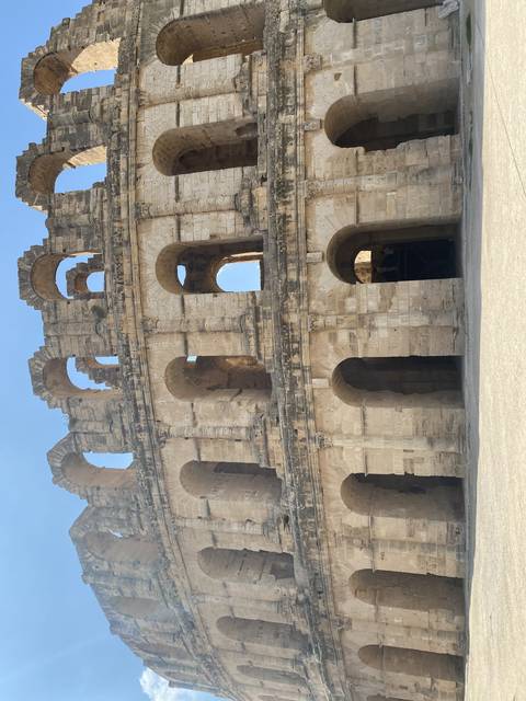 A large amphitheater structure with stone arches and bright sky.