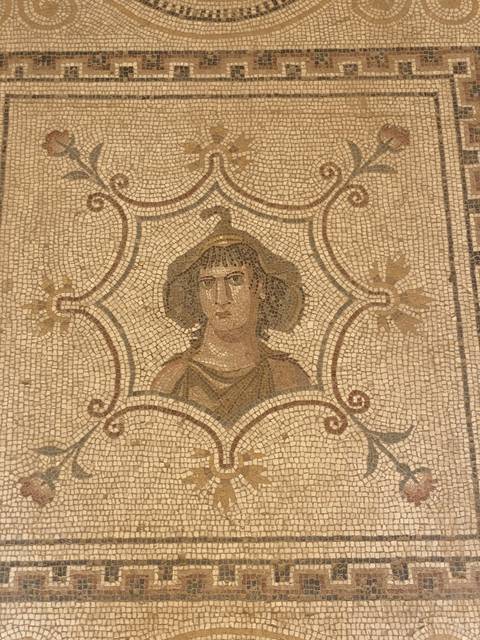 Mosaic depicting a historical figure on an intricate patterned background.