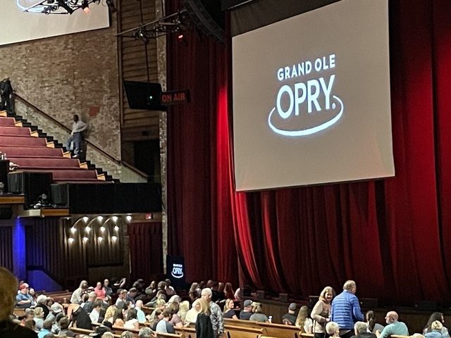      Interior of a theater with a stage and audience. 'Grand Ole Opry' displayed on a screen.
  