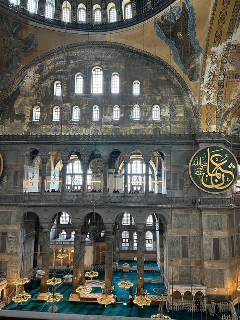       Interior of a grand mosque with intricate details and chandeliers.
  
