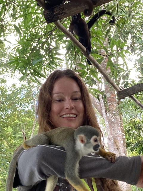 Woman holding a sloth with tropical foliage in the background.