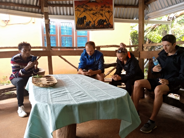 Four people sitting around a table indoors, checking their phones.