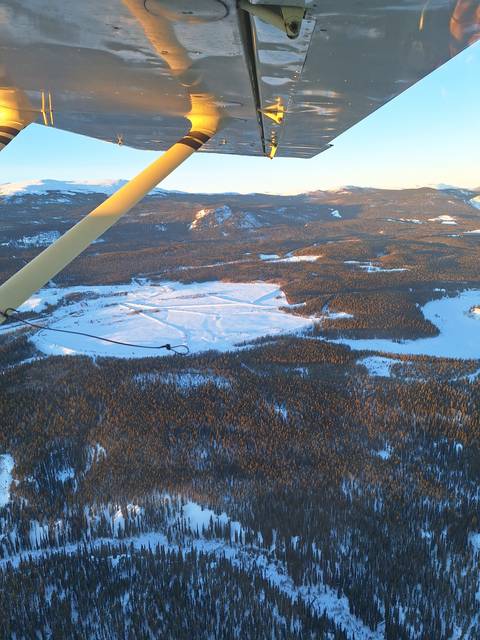Aerial view of a snowy forest landscape with visible aircraft wing.