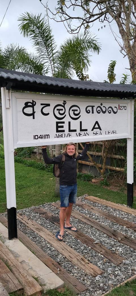       A person posing next to a sign for Ella, Sri Lanka.
  