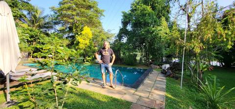       A person standing by a pool with lush greenery.
  