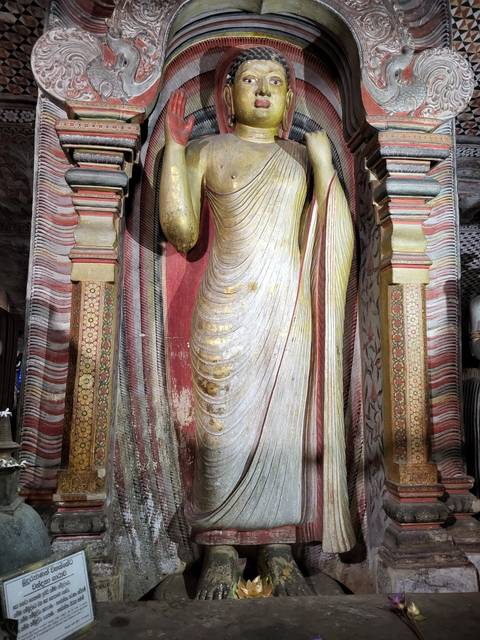       A standing Buddha statue inside a decorated temple.
  
