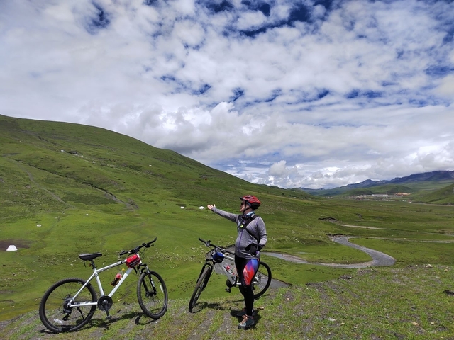       Person on a bike in a hilly green landscape.
  