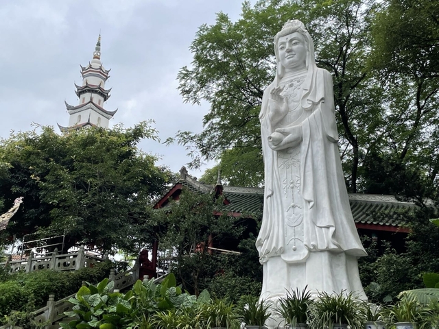       Statue in front of a pagoda surrounded by trees.
  