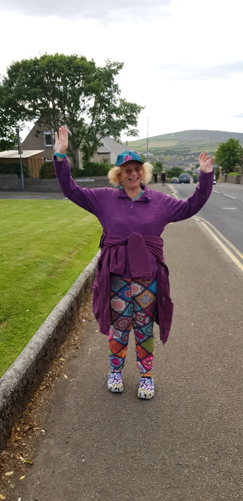       Person raising arms in a colorful outfit on a street.
  