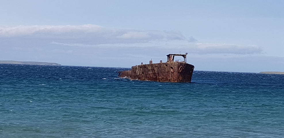Rusty shipwreck partially submerged in the sea.