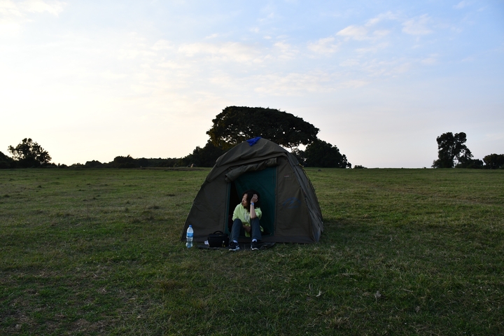       Camper enjoying the view outside a tent on a grassy plain.
  