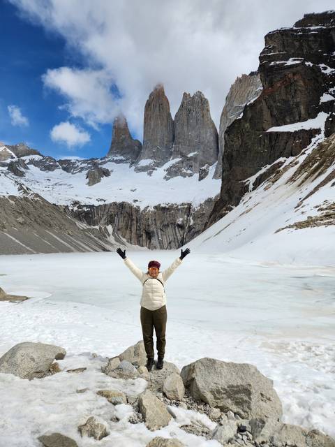 Person posing on snowy terrain with towering peaks in the background.