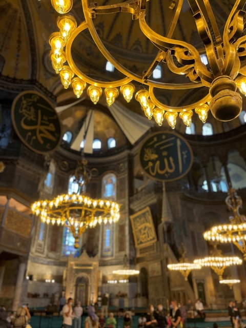 Interior of a historic mosque with chandeliers and arabic calligraphy.