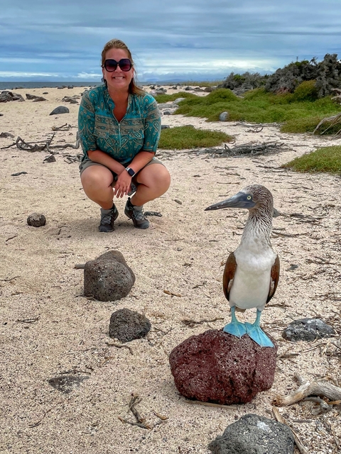       Person posing with a blue-footed booby on the beach.
  