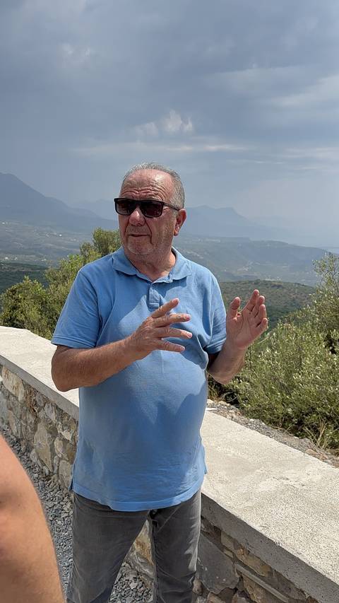       Man gesturing with hands against a mountain backdrop.
  