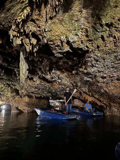       People on a boat inside a cave with rock formations overhead.
  