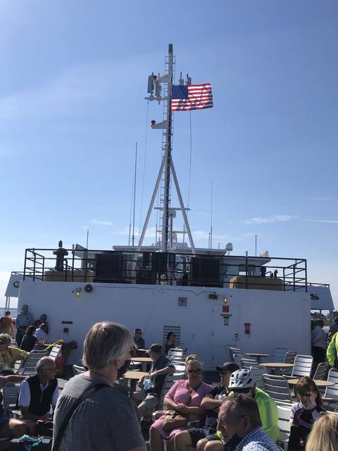People seated on the upper deck of a ferry with an American flag.